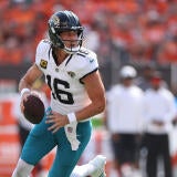 Jaguars QB Trevor Lawrence, in a white jersey and green pants, runs with the football.