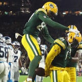 Josh Jacobs, in a green Packers jersey, celebrates his touchdown with his hands locked behind his back. Another Packers player jumps behind him to celebrate.