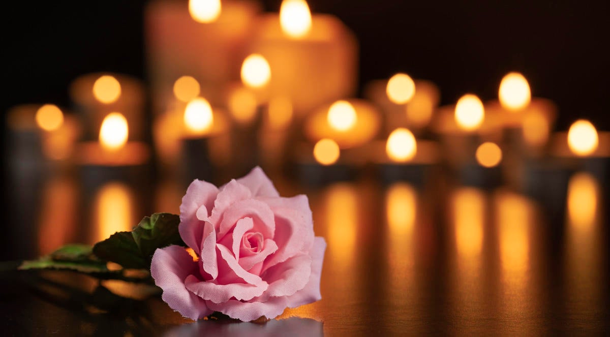 PINK ROSE ON THE GRAVE AND LIGHTED CANDLES UNFOCUSED IN THE BACKGROUND.