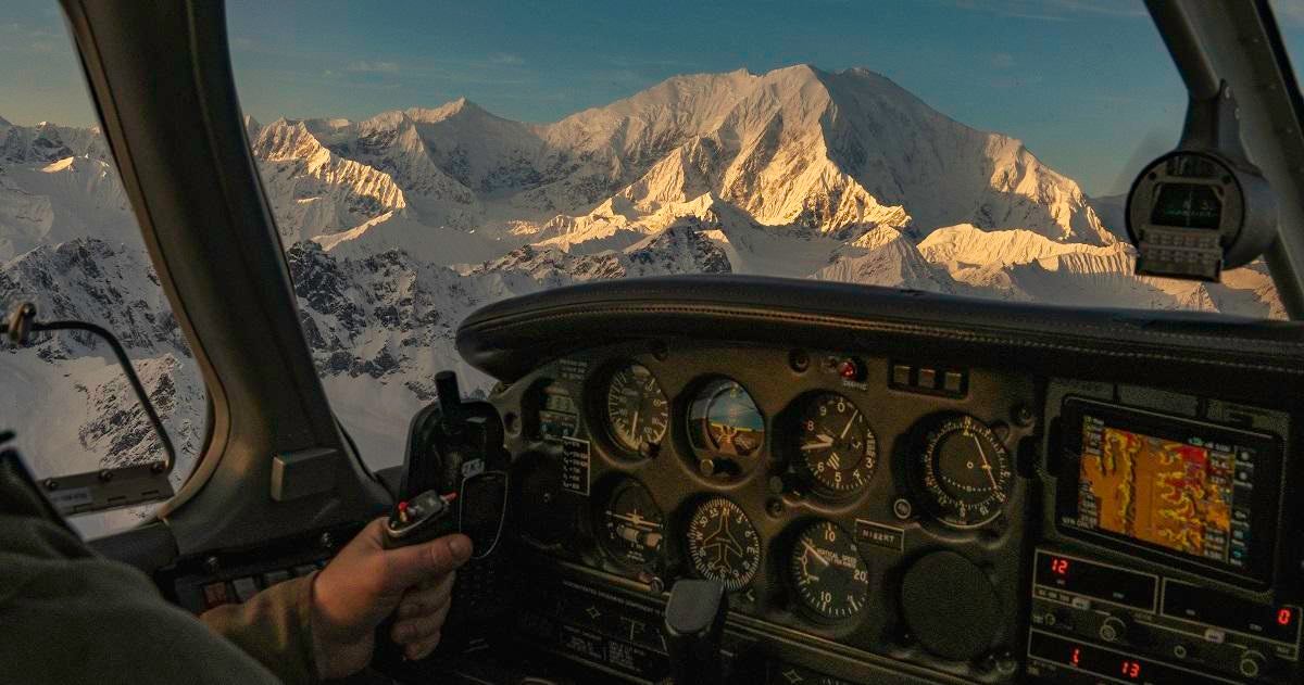 Man flies a small airplane at sunset with alpenglow on mount Foraker