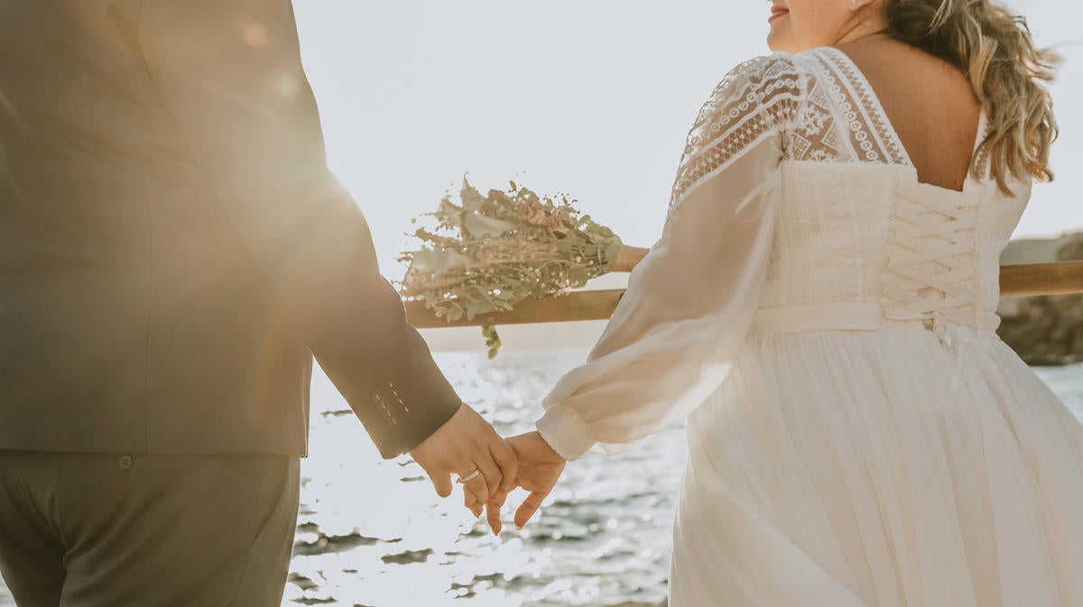 Close up view of a bride and groom holding hands while standing outdoors on sea coast.