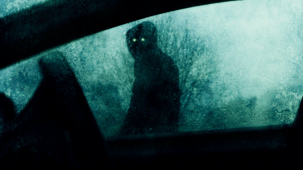 A horror concept of a spooky supernatural figure with glowing eyes. Looking into a car window on a stormy winters evening. With a blurred, textured ed