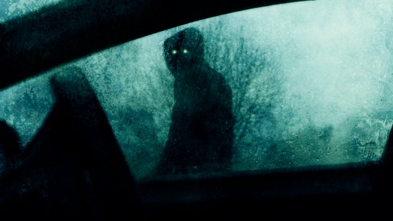 A horror concept of a spooky supernatural figure with glowing eyes. Looking into a car window on a stormy winters evening. With a blurred, textured ed