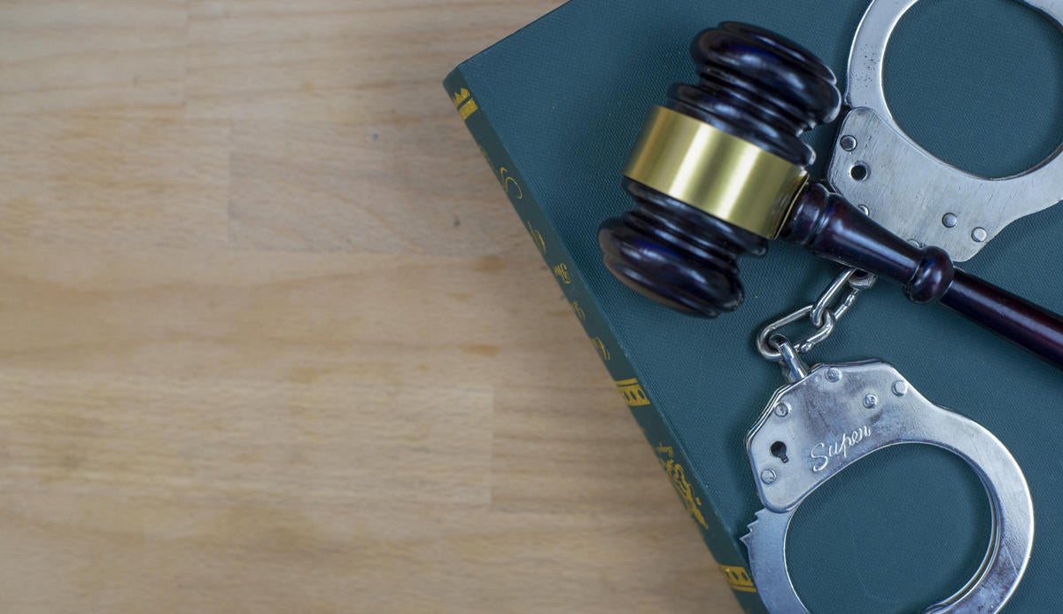 Gavel And Handcuffs On The Law Book Over The Wooden Table Background