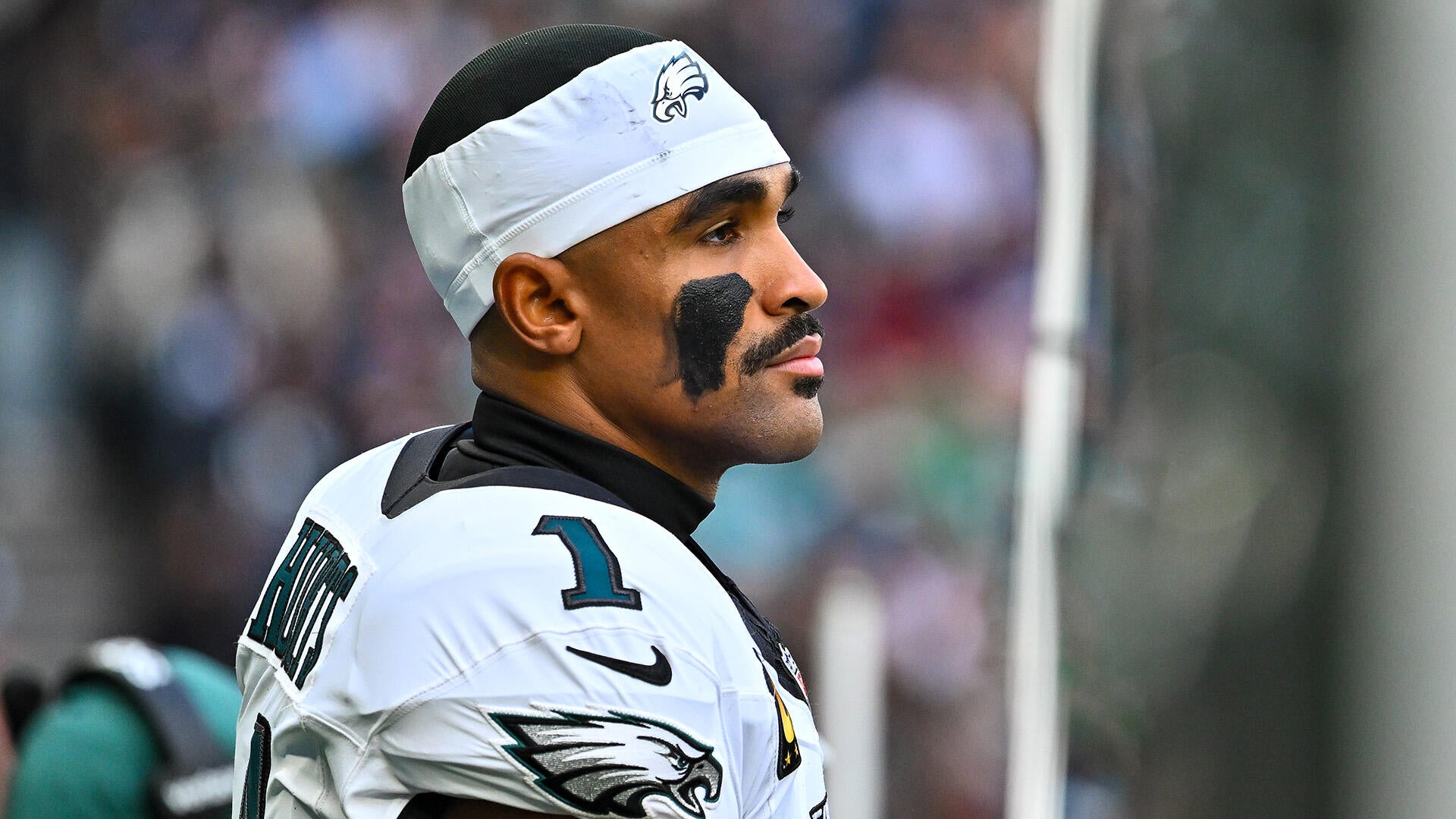 Eagles QB Jalen Hurts wears a white jersey and white sweatband on his head while looking out into the distance with his helmet off.