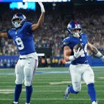 Two New York Giant players in blue jerseys celebrate as number 44 Cam Skattebo scores a touchdown.