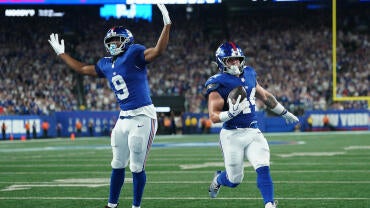 Two New York Giant players in blue jerseys celebrate as number 44 Cam Skattebo scores a touchdown.