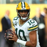 Packers' QB Jordan Love, in a number 10 jersey, holds the football and looks downfield during a play.
