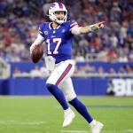 Bills QB Josh Allen, wearing a blue number 17 jersey, runs out of the pocket holding a football and points downfield.