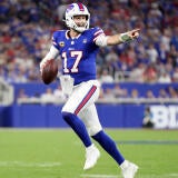 Bills QB Josh Allen, wearing a blue number 17 jersey, runs out of the pocket holding a football and points downfield.