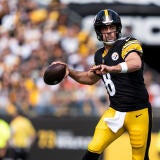 Steelers QB Aaron Rodger, wearing a black number 8 jersey, runs and attempts a pass with the football.