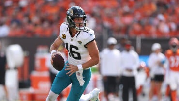 Jaguars QB Trevor Lawrence, in a white jersey and green pants, runs with the football.