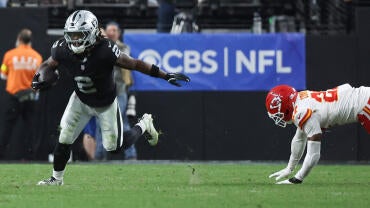 Raiders RB Ashton Jeanty, wearing number 2, runs with the football while a Kansas City Chiefs player dives after him.