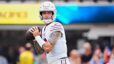 Carson Beck, wearing a white Cardinals helmet and jersey, drops back and looks to pass a football during warm ups.