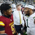 Commanders' Jayden Daniels, wearing a red Washington Jersey, and Micah Parsons, in a Green Bay jersey, shake hands and talk face to face.