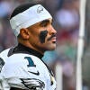 Eagles QB Jalen Hurts wears a white jersey and white sweatband on his head while looking out into the distance with his helmet off.