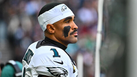 Eagles QB Jalen Hurts wears a white jersey and white sweatband on his head while looking out into the distance with his helmet off.