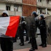 A protester holding a French flag stands in front of several masked police officers holding shields.