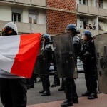 A protester holding a French flag stands in front of several masked police officers holding shields.