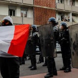 A protester holding a French flag stands in front of several masked police officers holding shields.