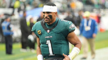 Eagles QB Jalen Hurts wears a white jersey and white sweatband on his head while looking out into the distance with his helmet off.